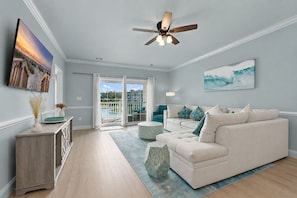 A living room with a white sofa, a ceiling fan, a TV, and a painting of waves.