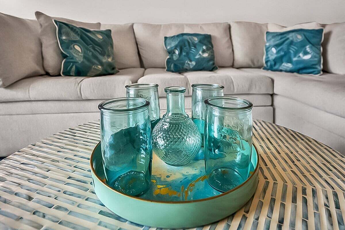 Ett turkosfärgat glasbricka med flera glas på ett vävt bord, placerat på en soffa med mönstrade kuddar.