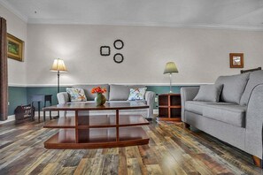 Uma sala de estar com uma mesa de centro de madeira, dois sofás cinzas e um abajur.