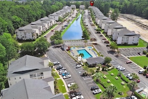 An aerial view of a hotel with a swimming pool, parking lots, and a river running through the property.