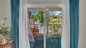 Ein Zimmer mit einer Schiebeglastür, die auf einen Balkon mit Blick auf einen Swimmingpool und Grünflächen führt.
