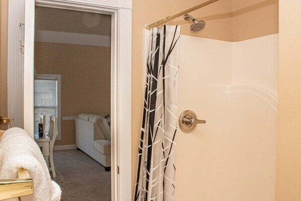 A bathroom with a shower, a towel rack, and a door leading to another room.