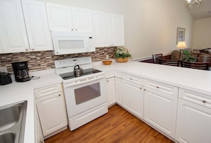 A kitchen with white cabinets, a microwave, stove, and a coffee maker. - Quiet 2BR Near Myrtlewood Golf Overlooking Pool (Myrtle Beach)