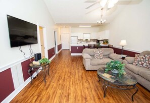A living room with a sofa, coffee table, and TV. There is a kitchen in the background. - Quiet 2BR Near Myrtlewood Golf Overlooking Pool (Myrtle Beach)