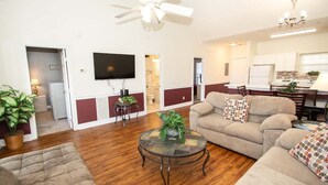 A living room with a sofa, a coffee table, and a television. There is a ceiling fan and a chandelier.
