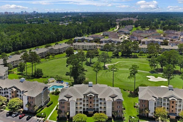 Um hotel de vários andares com um pátio central, rodeado por vegetação exuberante e um campo de golfe.