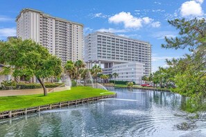 A hotel with a large water feature in front, surrounded by greenery and modern buildings. - Beautiful Two-Story Condo Steps From The Beach! (Myrtle Beach)