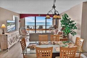 A dining area with a glass table, wooden chairs, and a view of the ocean.