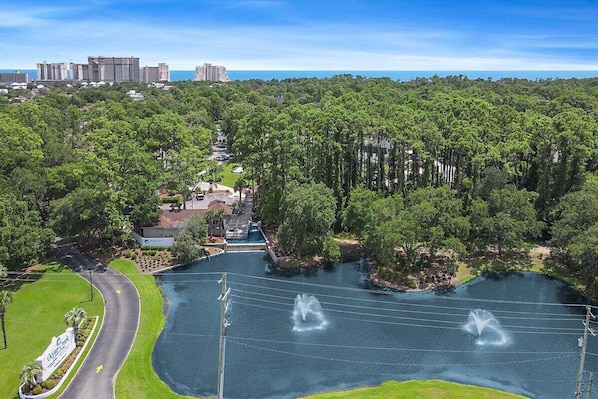 A large body of water with fountains, surrounded by dense greenery and a road curving around it.