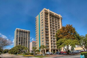 A high-rise hotel with multiple floors, balconies, and a parking area with cars. - Comfortable & Cozy 1Br Condo- Close to Beach! (Myrtle Beach)