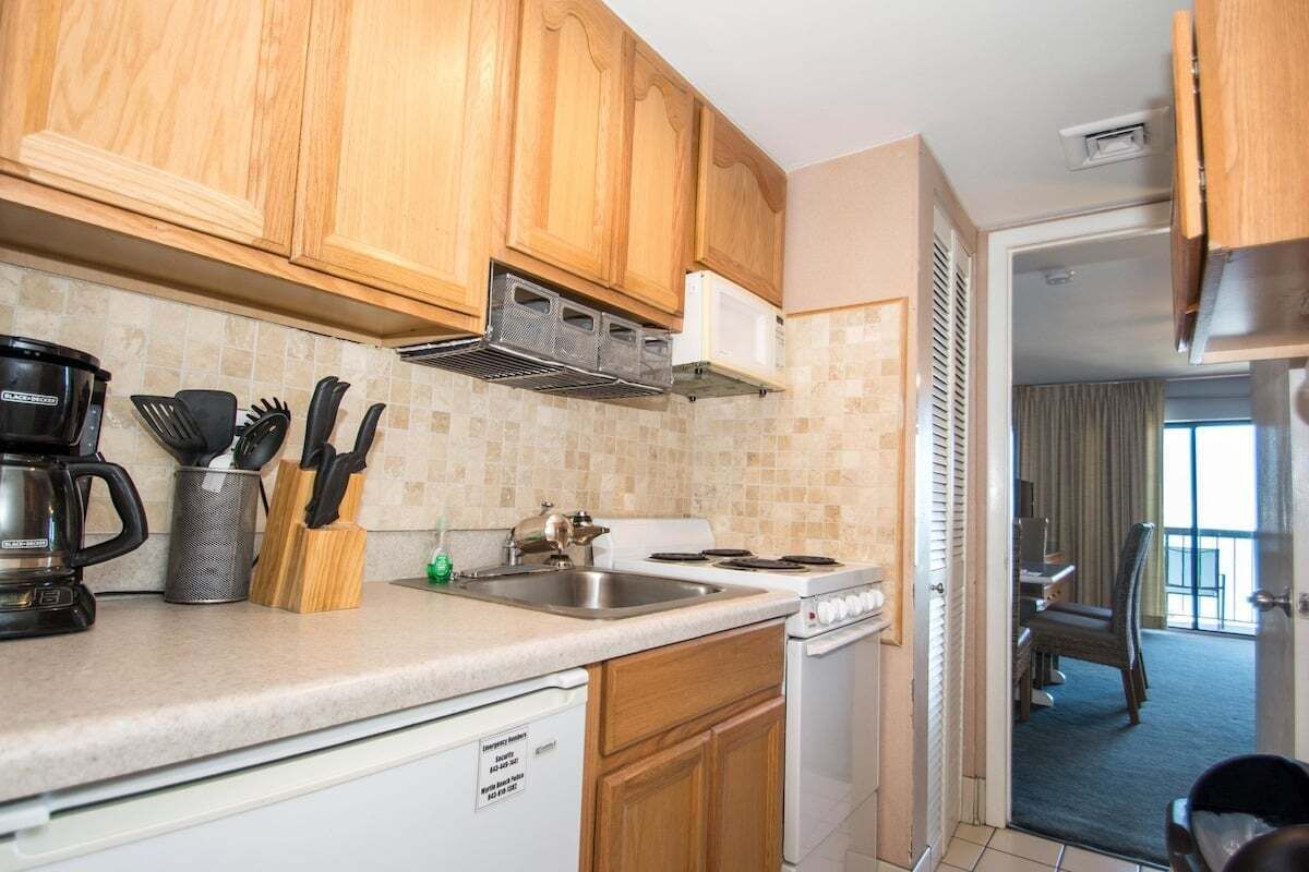 A kitchen with wooden cabinets, a coffee maker, a kettle, and a sink.