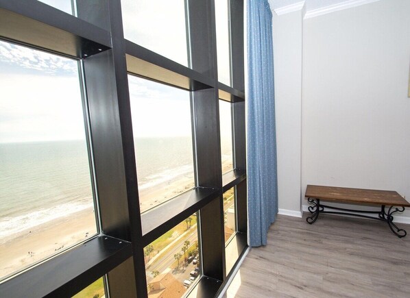 A room with large windows overlooking a beach, a wooden bench, and a light-colored floor. - 2 level Oceanview Penthouse across from ocean! (Myrtle Beach)