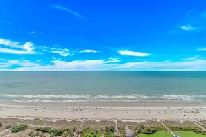 A beach with a clear sky, calm sea, and a sandy shore with umbrellas.