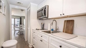 A modern kitchen with white cabinetry, a stainless steel sink, a microwave, and a wooden cutting board. - 1Br/1Ba MB Condo! Sleeps 6! Steps To The Ocean! (Myrtle Beach)