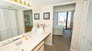 A hotel bathroom with a large mirror, vanity, and a view of the balcony.
