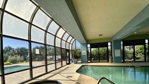 Una piscina interior con paredes de vidrio transparente, un jacuzzi y una escalera de piscina.
