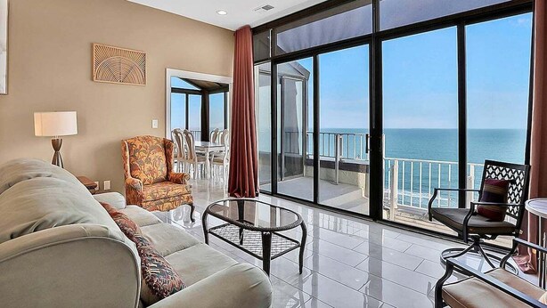 Un salon spacieux doté d’une grande fenêtre donnant sur la mer, avec un canapé, un fauteuil et une petite table.