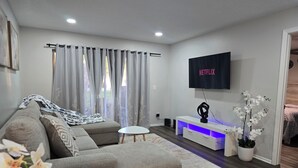 Un salon moderne avec un canapé d’angle gris, une table basse blanche, un téléviseur fixé au mur et un petit meuble blanc doté d’un éclairage LED bleu.