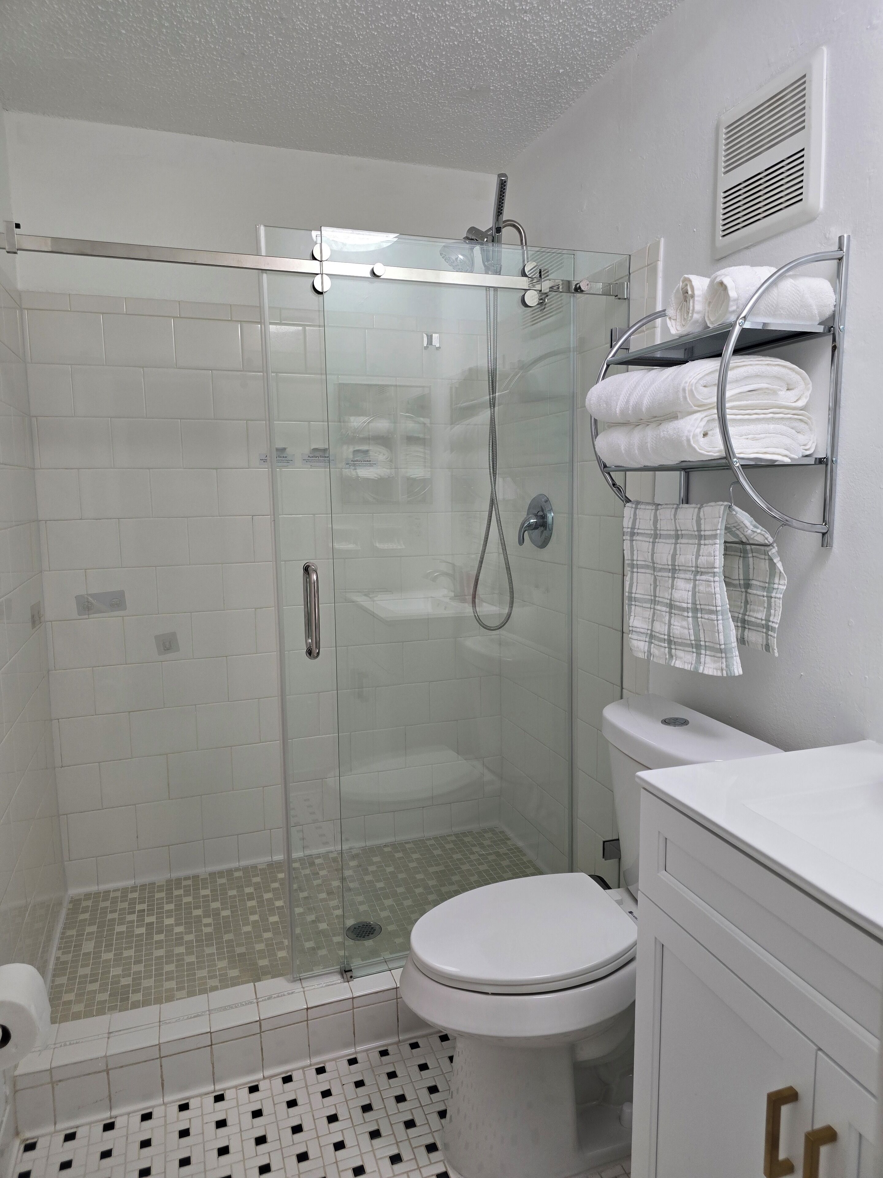 Une salle de bain moderne avec une douche à parois de verre, des murs recouverts de carreaux blancs, des toilettes blanches et un porte-serviettes avec des serviettes soigneusement pliées.