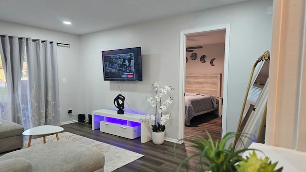 Un salon moderne avec un téléviseur à écran plat, un meuble de rangement blanc, un canapé gris et une petite table blanche.