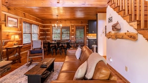 Interior acogedor de una cabaña con escalera de madera, zona de comedor y sala de estar con sofá de cuero.