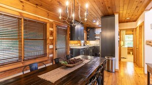 Un interior de madera con una mesa de comedor, sillas, una araña y una zona de cocina.