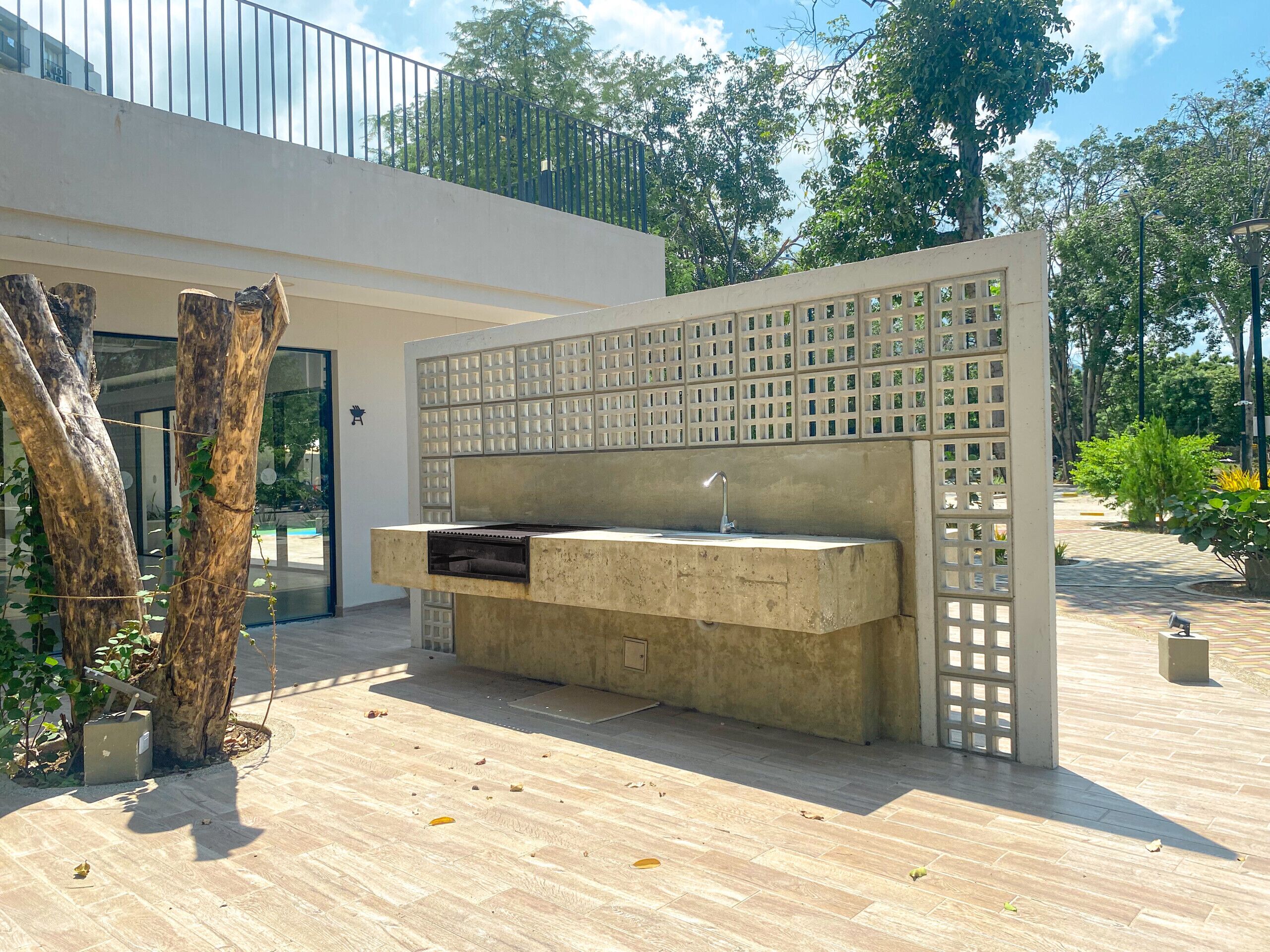 An outdoor kitchen area with a concrete countertop, a sink, and a wooden tree trunk nearby.