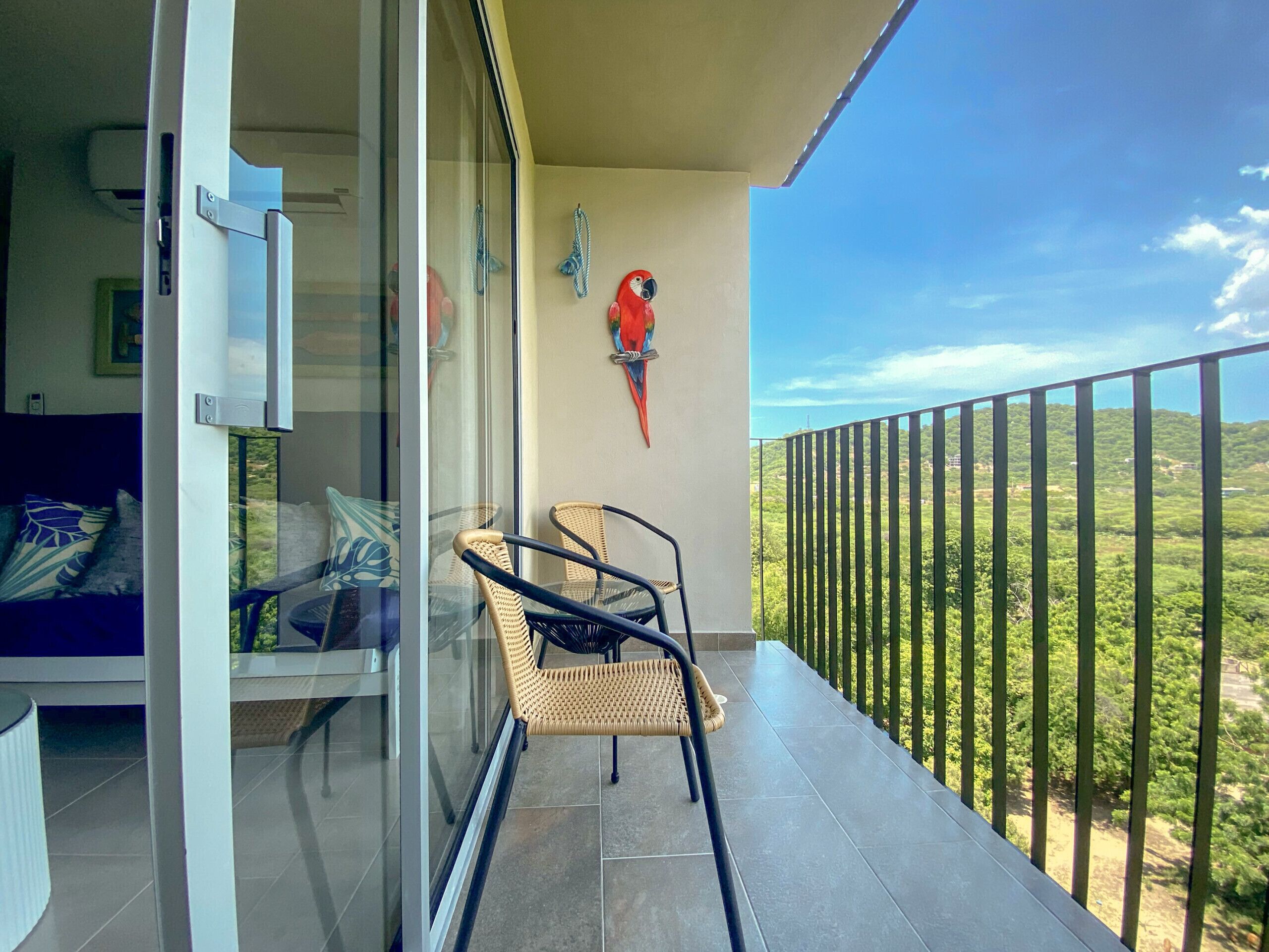 A balcony with wicker chairs, a glass door, and a view of a green landscape.