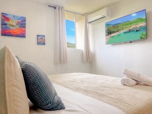 Quarto com cama, almofadas, televisão e janela com cortinas.