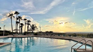 A swimming pool with lounge chairs and palm trees, overlooking a body of water. - 🌸CBC 1-9F -Gulf front condo with amazing views and a heated Pool! (Clearwater Beach)