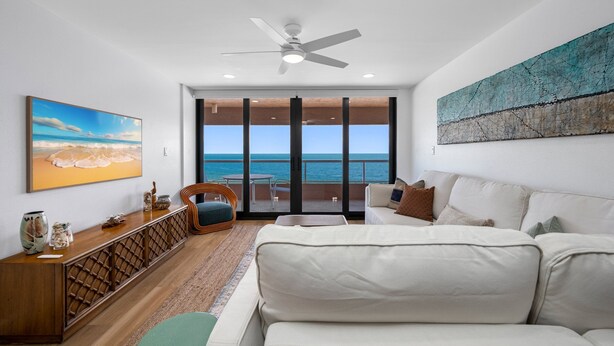 A modern living room with a large white sofa, a wooden console table, and a view of the ocean through large sliding doors. - 🌸CBC 1-9F -Gulf front condo with amazing views and a heated Pool! (Clearwater Beach)