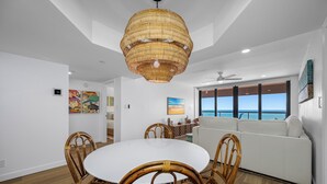 A dining area with a round table and wicker chairs, a white sofa, and a large window overlooking the ocean. - 🌸CBC 1-9F -Gulf front condo with amazing views and a heated Pool! (Clearwater Beach)