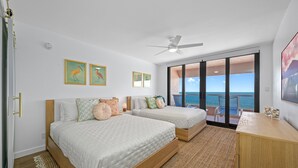 A bedroom with two beds, a ceiling fan, and a view of the ocean through large sliding doors. - 🌸CBC 1-9F -Gulf front condo with amazing views and a heated Pool! (Clearwater Beach)