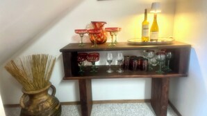 A wooden wine display table with various wine glasses and bottles, a decorative sign above it, and a vase with straw on the floor beside it. - Book now for great fall colors…watch wildlife from deck! (Angel Fire)