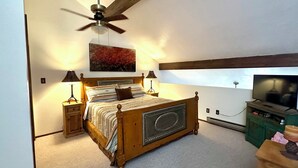A bedroom with a wooden bed, a ceiling fan, a painting, two bedside lamps, a television, and a green cabinet. - Book now for great fall colors…watch wildlife from deck! (Angel Fire)