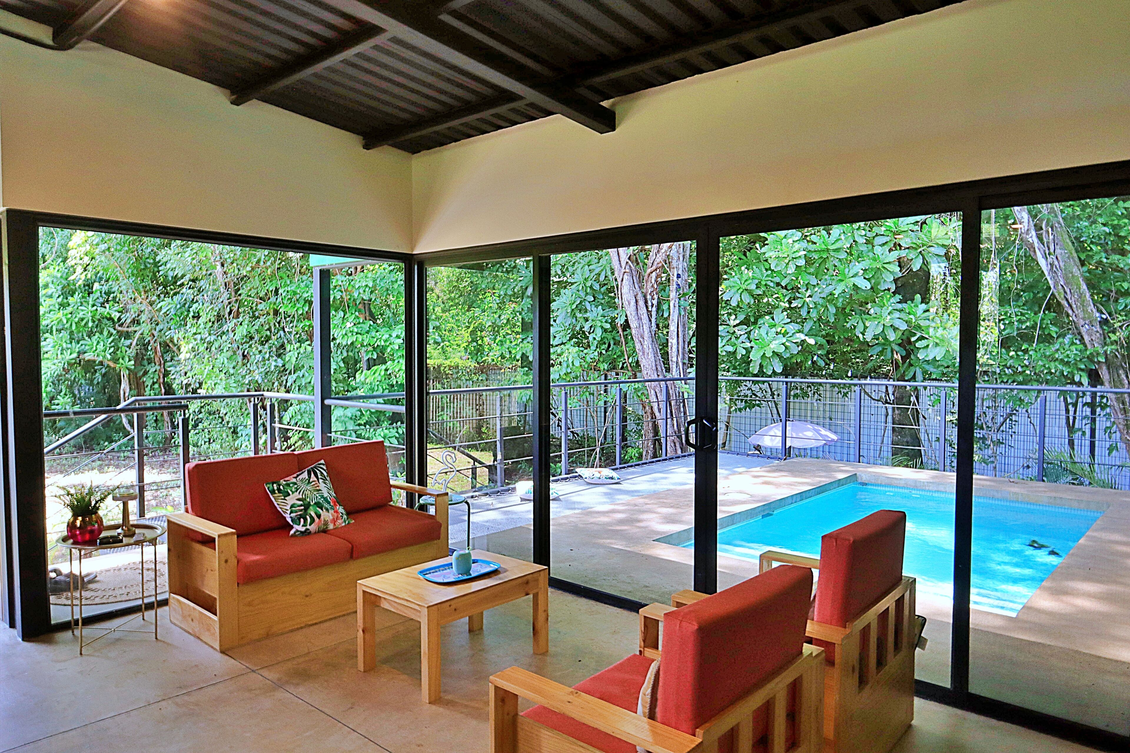 A room with a large glass wall, a pool, and outdoor furniture.