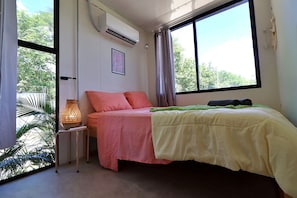 A bedroom with a bed, a bedside lamp, a window, and an air conditioning unit.
