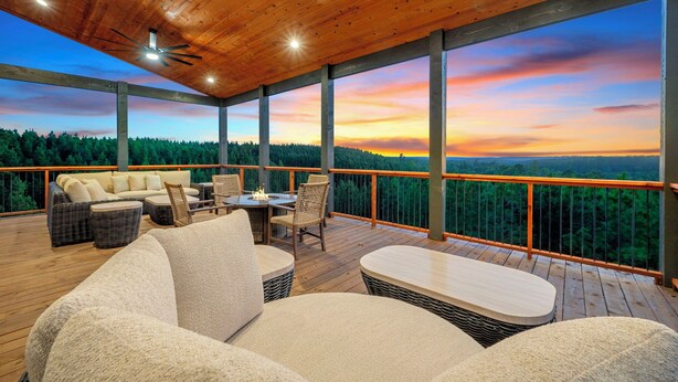 A covered outdoor deck with a wooden ceiling, furnished with sofas, chairs, and a table. - The Unicorn - Featured on Staycation: Luxury Broken Bow Retreat (Broken Bow)