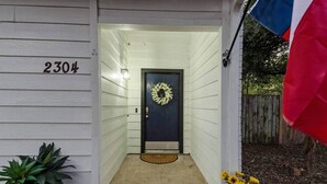 Una casa con una puerta delantera oscura, un adorno de bienvenida en la puerta y el número 2304 en la pared.