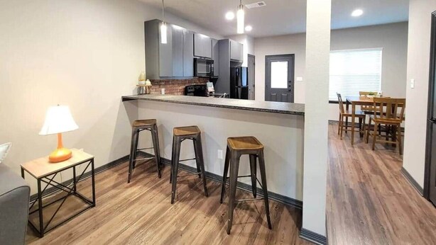 A modern kitchen with a bar area, wooden flooring, and a dining area with chairs.