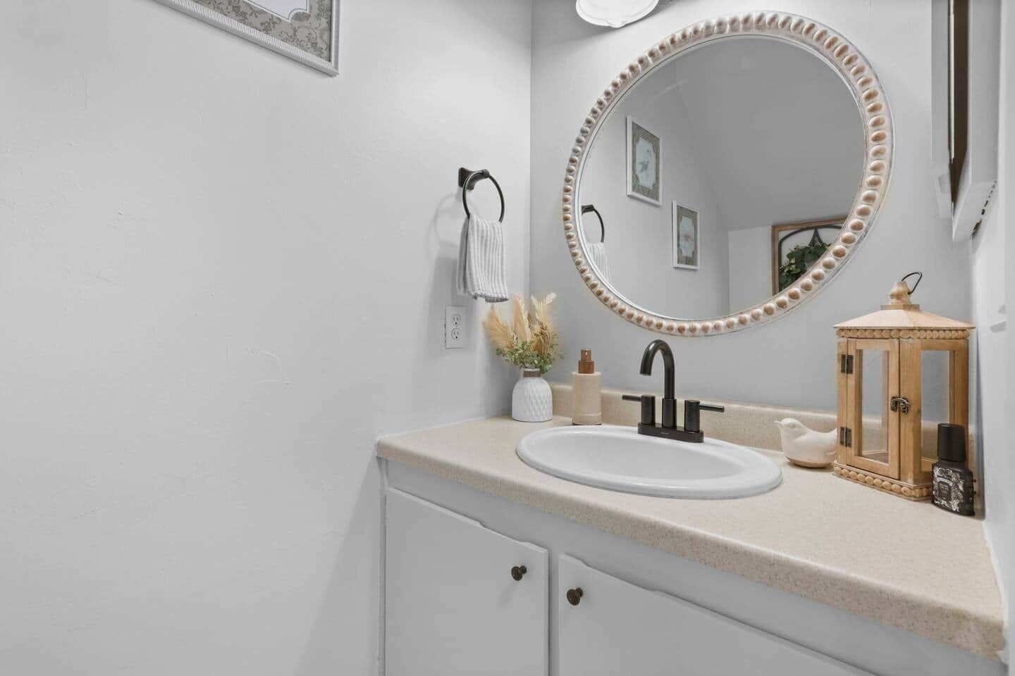 A bathroom with a white sink, a round mirror with a decorative frame, a towel rack, and a small wooden cabinet.