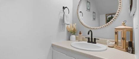 A bathroom with a white sink, a round mirror with a decorative frame, a towel rack, and a small wooden cabinet.