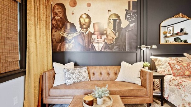 Uma sala de estar com um sofá marrom, uma mesa de centro com uma planta e um mural grande com personagens de Star Wars.