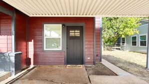 Uma casa vermelha com porta cinza escura, uma janela e um caminho de acesso de concreto.