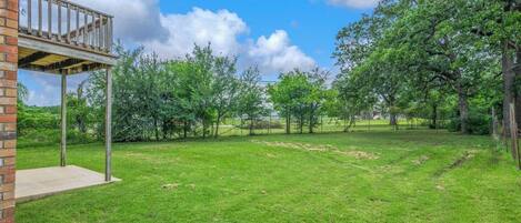 A backyard with a wooden deck, a brick wall, and a grassy lawn with trees.
