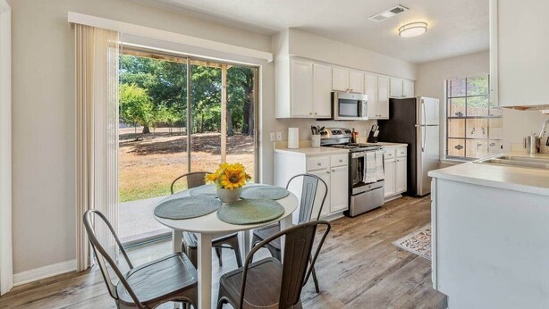 Una cocina moderna con armarios blancos, un refrigerador de acero inoxidable y un comedor con mesa y sillas.