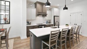 Une cuisine moderne dotée d’un îlot central, de meubles blancs et d’un coin repas avec des chaises en bois.