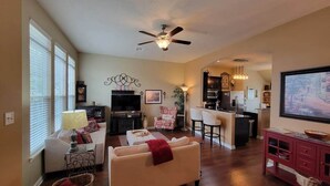A spacious living room with a sofa, a TV, and a dining area with a kitchen in the background.