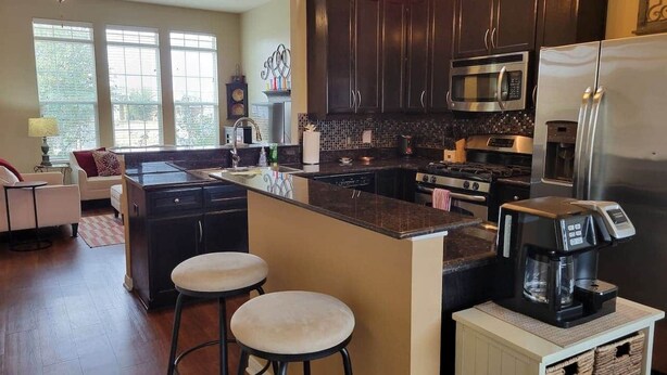 A kitchen with dark wooden cabinets, a central island with stools, a refrigerator, a stove, and a coffee maker.