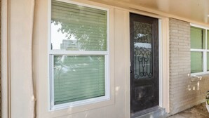 A house with a green window, a black door with a decorative glass panel, and a brick wall. - Northgate Apartment - 1 block to TAMU! (College Station)